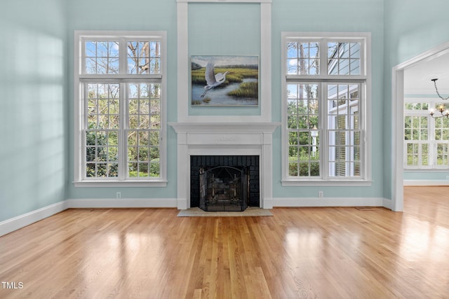 unfurnished living room featuring baseboards, a brick fireplace, wood finished floors, and an inviting chandelier