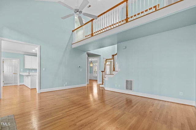 unfurnished living room with stairway, baseboards, visible vents, and light wood-type flooring