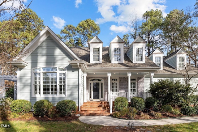 new england style home with brick siding, covered porch, and a shingled roof