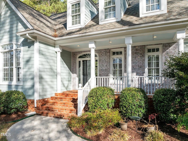 doorway to property featuring covered porch and a shingled roof