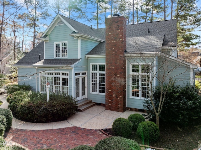 rear view of property featuring a shingled roof, entry steps, a chimney, french doors, and a patio area