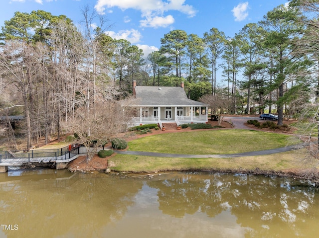 rear view of house with covered porch, a chimney, a yard, and a water view