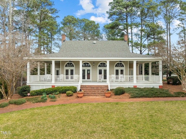 view of front facade featuring a shingled roof, a front lawn, covered porch, french doors, and a chimney