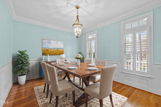 dining space with ornamental molding, wood finished floors, and wainscoting