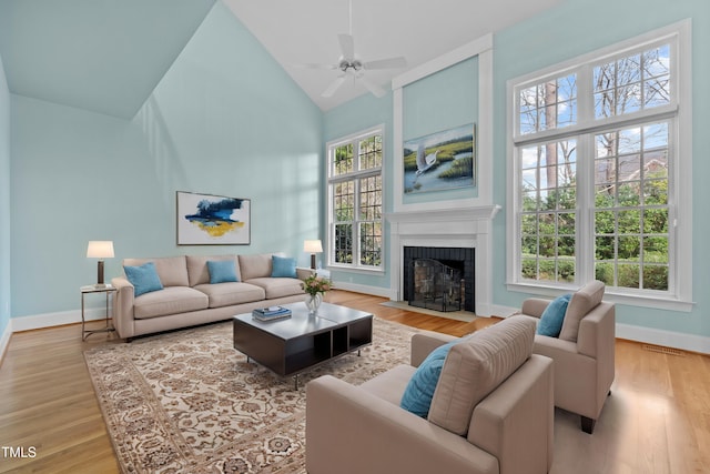 living room with visible vents, baseboards, a fireplace with flush hearth, light wood-type flooring, and high vaulted ceiling