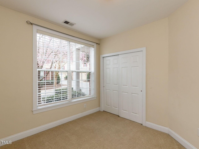 unfurnished bedroom with baseboards, visible vents, a closet, and light carpet