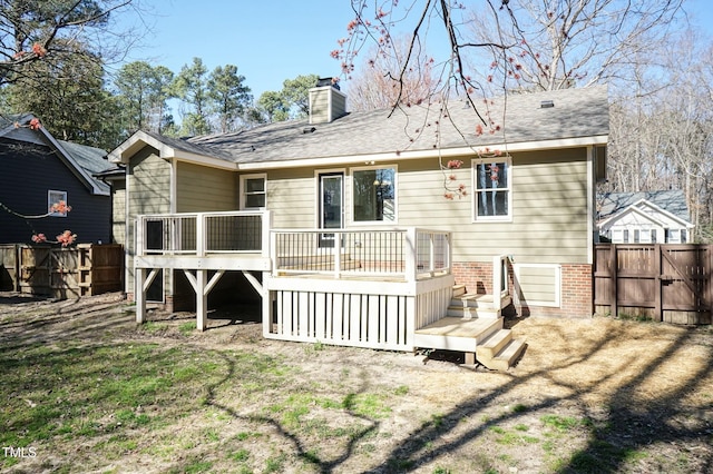 rear view of property with brick siding, fence, a wooden deck, roof with shingles, and a chimney