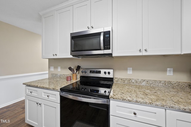 kitchen featuring black electric range, stainless steel microwave, light stone countertops, and white cabinetry