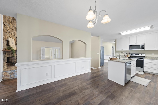 kitchen with a center island with sink, light stone counters, stainless steel appliances, white cabinets, and a chandelier