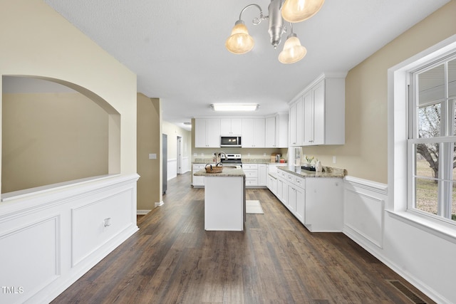 kitchen with dark wood finished floors, a notable chandelier, white cabinets, stainless steel appliances, and a kitchen island with sink