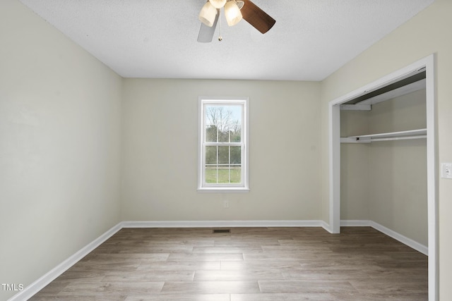 unfurnished bedroom with wood finished floors, baseboards, ceiling fan, a closet, and a textured ceiling