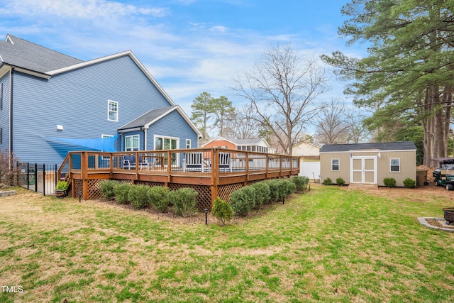 rear view of house with fence, a wooden deck, a lawn, an outbuilding, and a storage unit