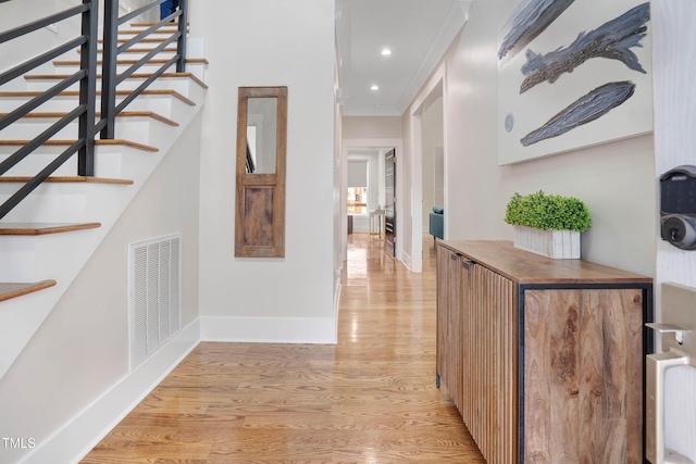 hallway featuring visible vents, light wood-style flooring, stairs, and ornamental molding