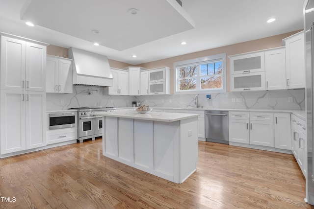 kitchen with custom exhaust hood, appliances with stainless steel finishes, white cabinets, and light wood finished floors