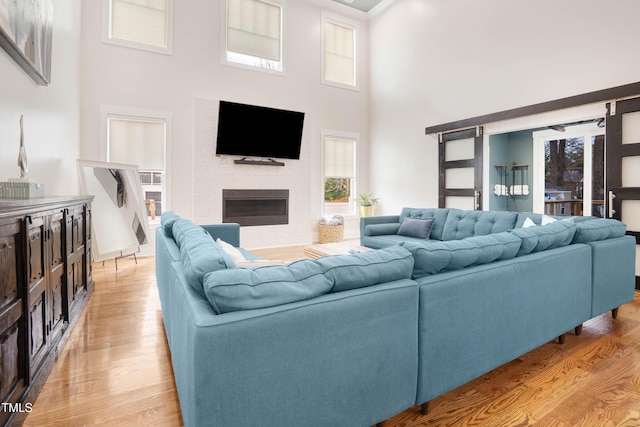 living area featuring light wood-type flooring, a glass covered fireplace, and a towering ceiling