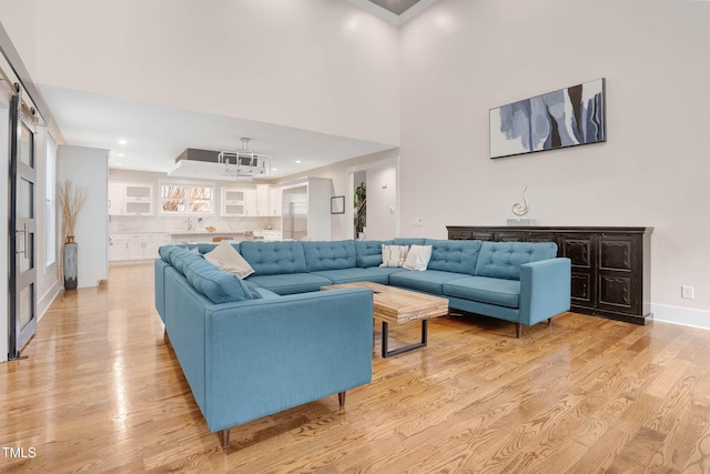 living area with recessed lighting, baseboards, light wood-type flooring, and a high ceiling