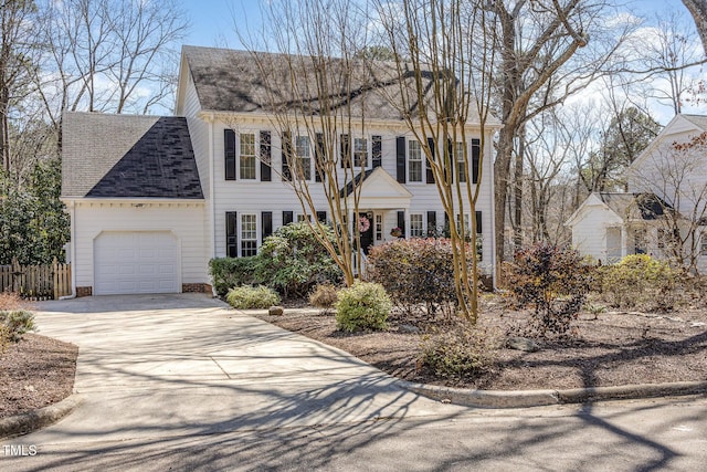 colonial home with an attached garage, driveway, roof with shingles, and fence