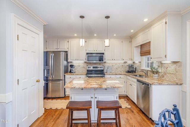 kitchen featuring light stone counters, light wood-style flooring, white cabinets, appliances with stainless steel finishes, and a center island