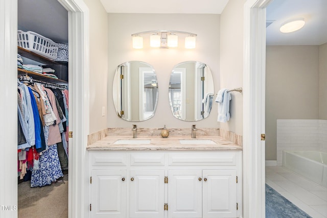 full bathroom with double vanity, a walk in closet, a garden tub, and a sink