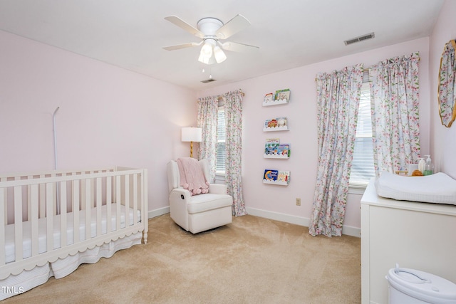 carpeted bedroom featuring visible vents, baseboards, a nursery area, and ceiling fan