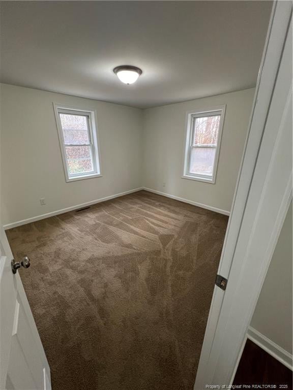 spare room featuring plenty of natural light, visible vents, baseboards, and dark colored carpet