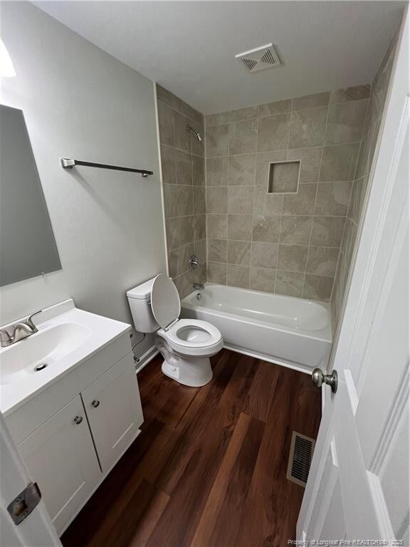 full bath featuring visible vents, toilet, wood finished floors, tub / shower combination, and vanity