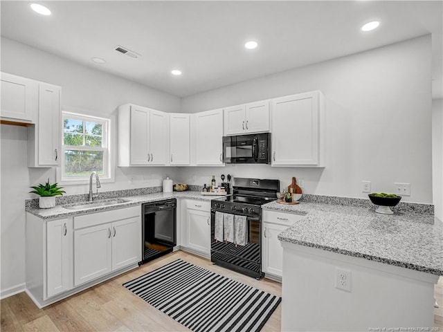 kitchen with white cabinets, light stone counters, a sink, a peninsula, and black appliances