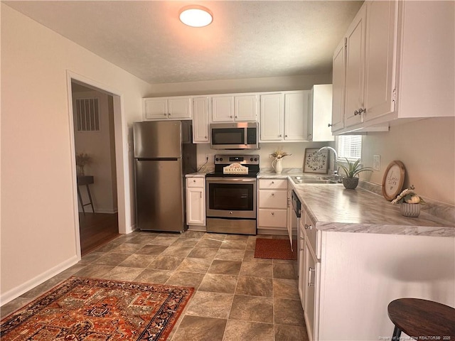 kitchen featuring a sink, white cabinetry, stainless steel appliances, light countertops, and baseboards