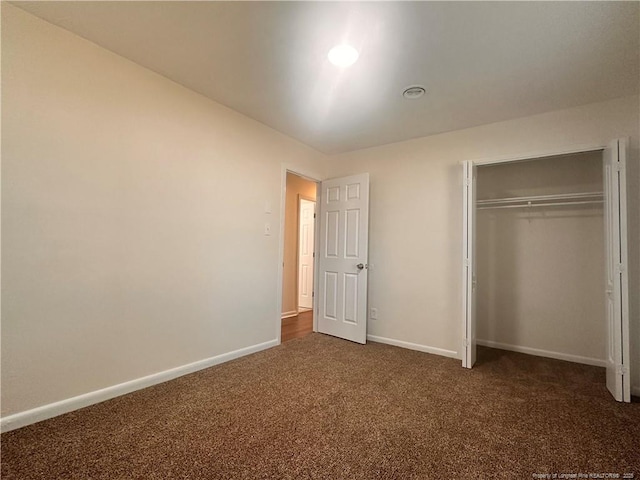 unfurnished bedroom featuring baseboards, dark colored carpet, and a closet