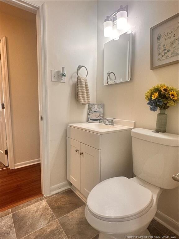 half bathroom featuring baseboards, toilet, vanity, and stone finish floor