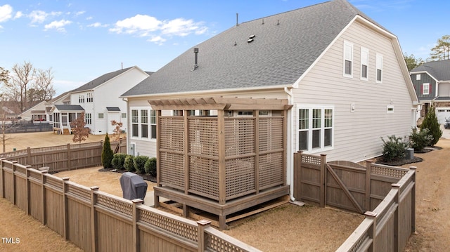 back of house with a gate, a fenced backyard, and a shingled roof