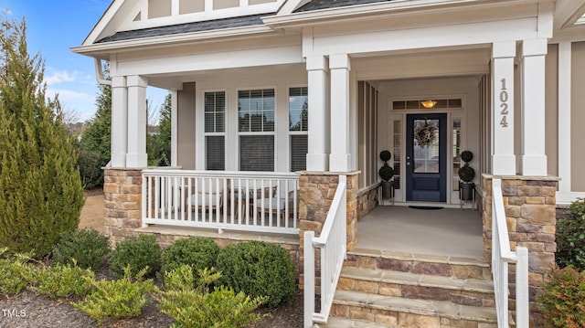 doorway to property featuring stone siding, covered porch, and a shingled roof