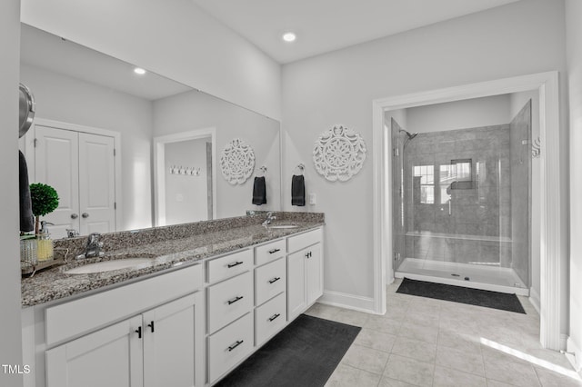 bathroom with a sink, baseboards, tiled shower, and double vanity