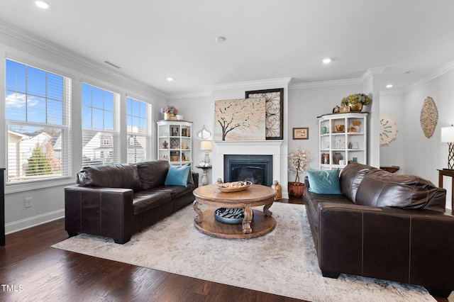 living room featuring wood finished floors, baseboards, recessed lighting, ornamental molding, and a glass covered fireplace