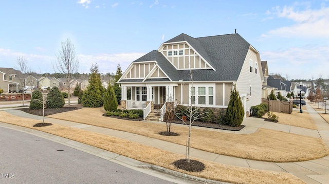 craftsman house with covered porch, stone siding, a residential view, and roof with shingles