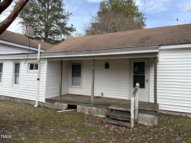 doorway to property with covered porch and a shingled roof