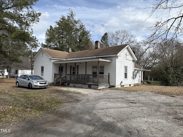 ranch-style house featuring covered porch, driveway, a chimney, and roof with shingles