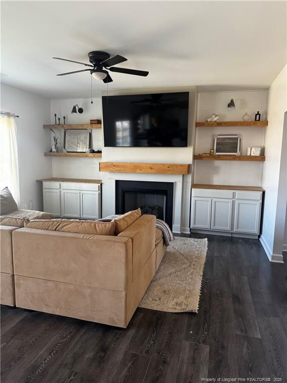 living room with baseboards, dark wood-type flooring, ceiling fan, and a fireplace