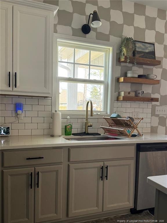 kitchen featuring a sink, open shelves, stainless steel dishwasher, light countertops, and decorative backsplash