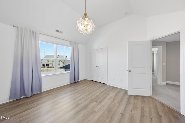 unfurnished bedroom featuring light wood-type flooring, visible vents, baseboards, lofted ceiling, and a chandelier