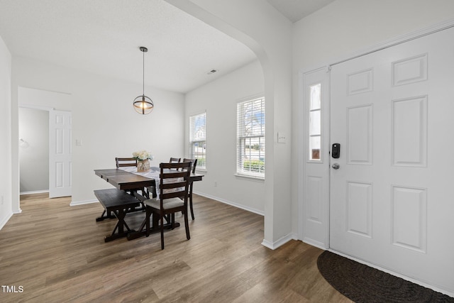 foyer with wood finished floors, arched walkways, and baseboards