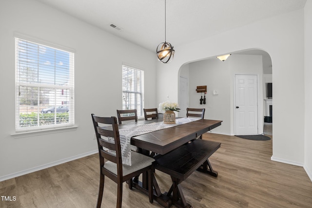 dining area with arched walkways, a healthy amount of sunlight, and wood finished floors