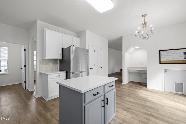 kitchen with light countertops, decorative backsplash, light wood-style flooring, freestanding refrigerator, and hanging light fixtures