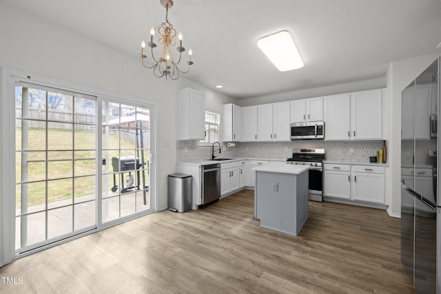 kitchen with a sink, wood finished floors, appliances with stainless steel finishes, light countertops, and decorative backsplash