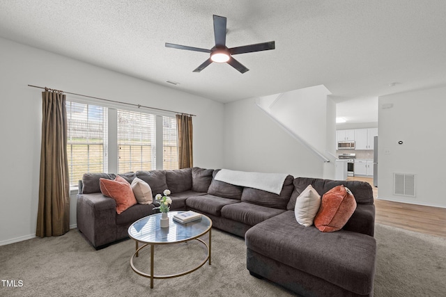 living room featuring a textured ceiling, ceiling fan, visible vents, and light carpet