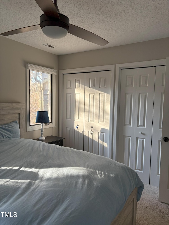 carpeted bedroom with visible vents, multiple closets, a textured ceiling, and ceiling fan