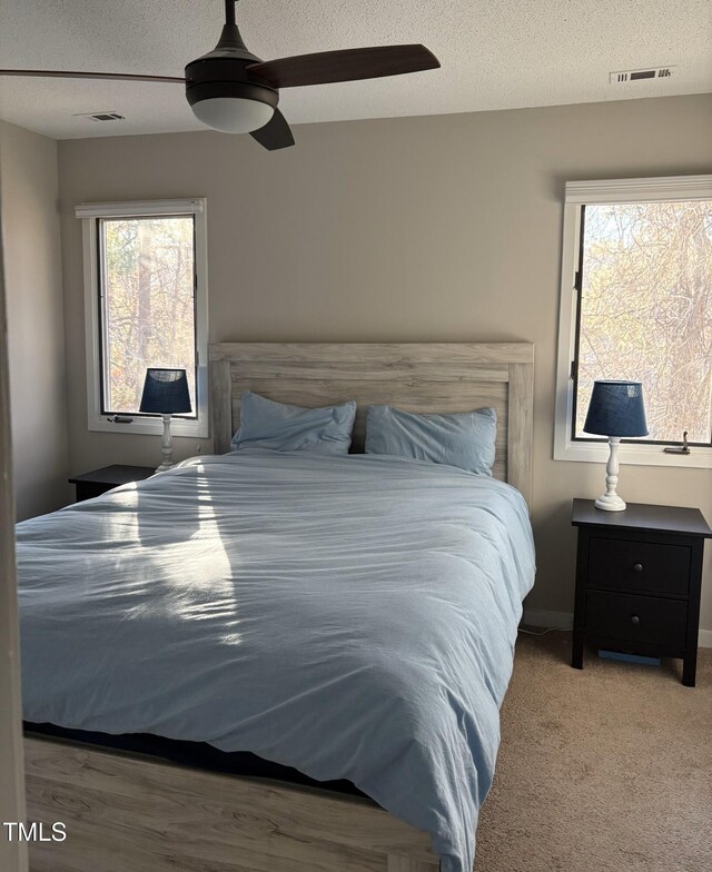 carpeted bedroom with visible vents, a textured ceiling, and ceiling fan