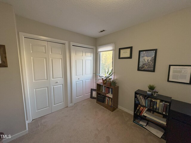 interior space featuring visible vents, baseboards, light colored carpet, and a textured ceiling