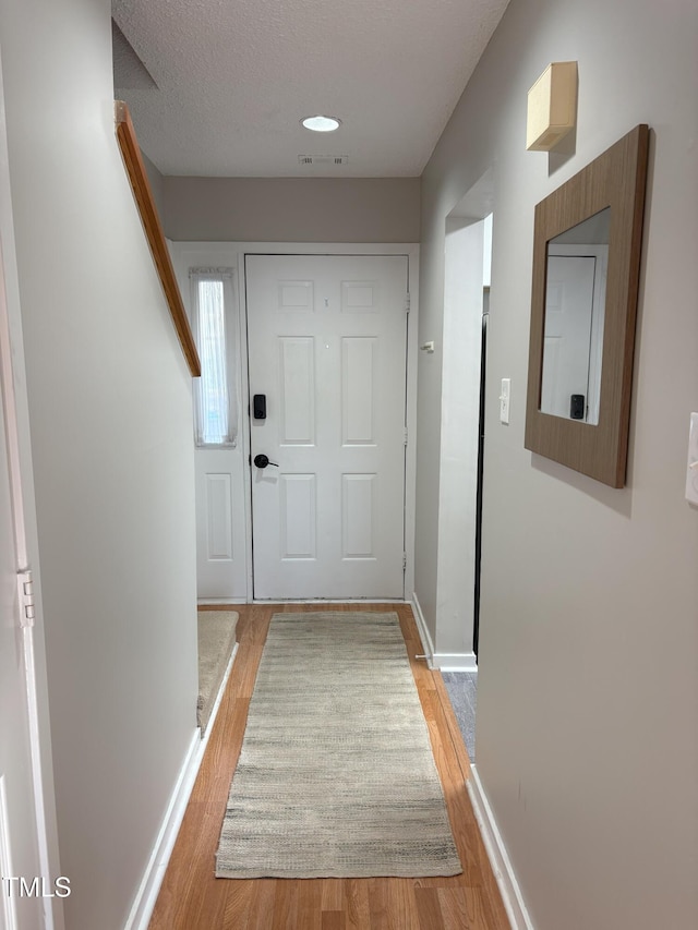 entryway with visible vents, a textured ceiling, baseboards, and light wood-style floors