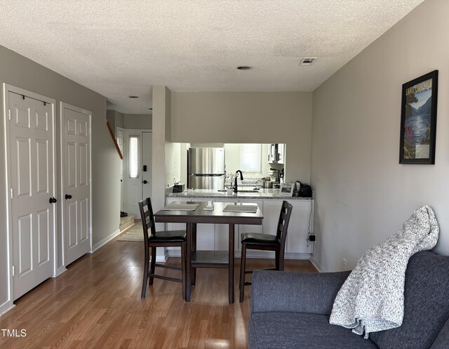 dining room featuring baseboards, wood finished floors, visible vents, and a textured ceiling